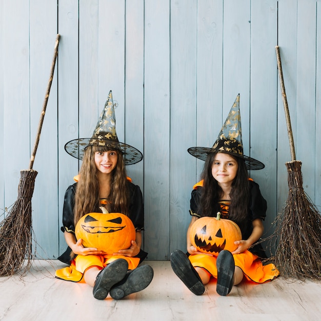 Pre-teen girls in witch costumes holding pumpkins and smiling