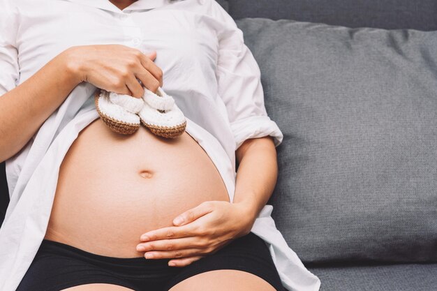 Pregnancy woman holding pair of shoes on her belly preparing baby product for her baby