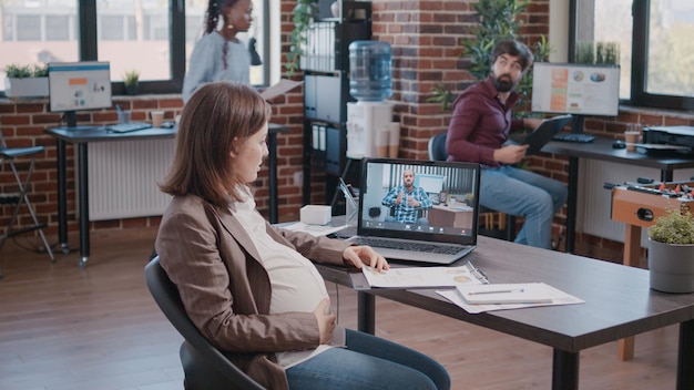 Free photo pregnant employee using video call to talk to manager about project planning and strategy. woman attending business meeting with colleague on video online conference, expecting child.