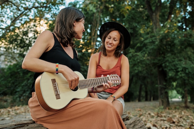 Free photo pregnant female with her partner playing the ukulele in a park while enjoying each others' company