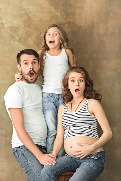 Pregnant mother with teen daughter and husband. Family studio portrait over brown wall