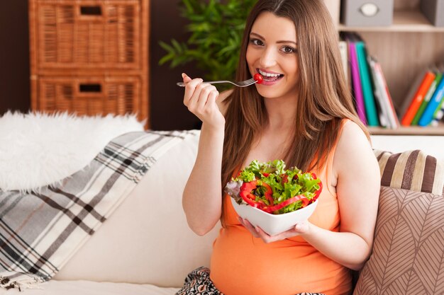 Pregnant smiling woman eating salad