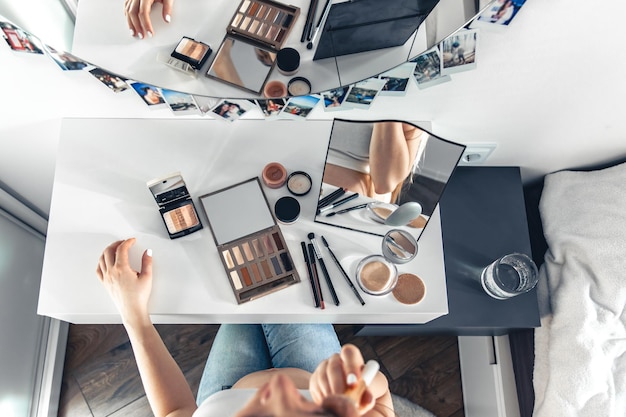 A pregnant woman applies makeup at home in front of a mirror