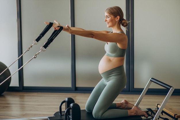 Pregnant woman exercising with the help of reformer on pilates class