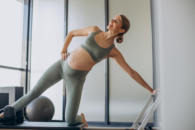 Pregnant woman exercising with the help of reformer on pilates class