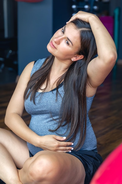 Free photo pregnant woman in the gym doing warmup sitting on a yoga mat