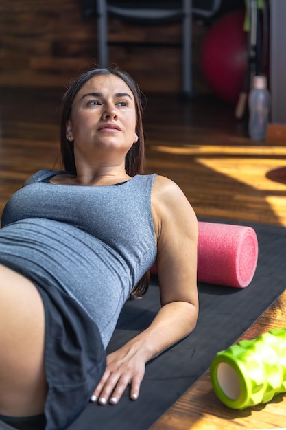 Free Photo pregnant woman in the gym on a mat with a massage roller