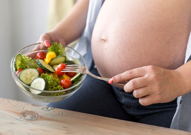 Pregnant woman holding bowl of salad close-up