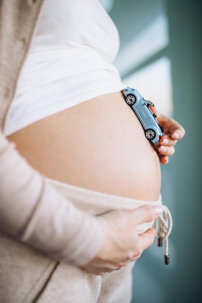 Pregnant woman holding small car model by the belly