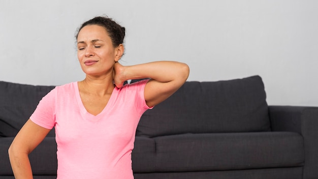 Free photo pregnant woman at home holding her neck while exercising