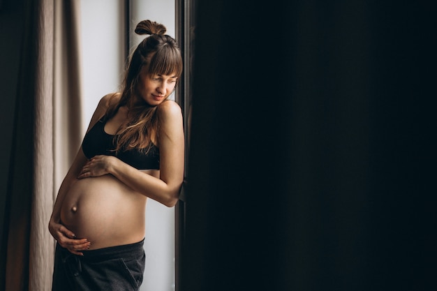 Free Photo pregnant woman standing by the window