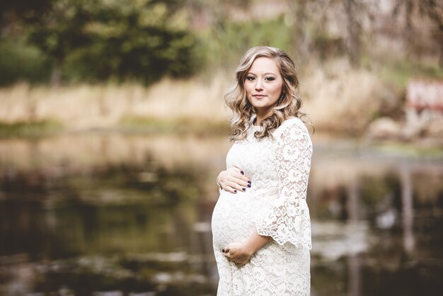 Pregnant woman wearing a white dress in a park with a lake