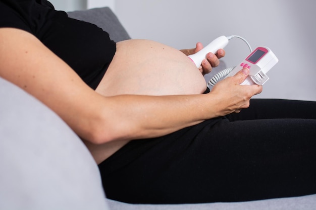 Free Photo pregnant woman with a fetal doppler listening to the baby39s heart sitting