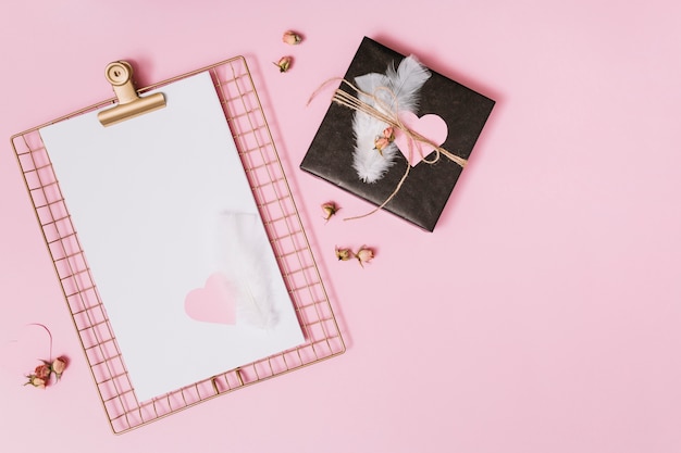 Present box with feathers and ornament heart near clipboard with paper 