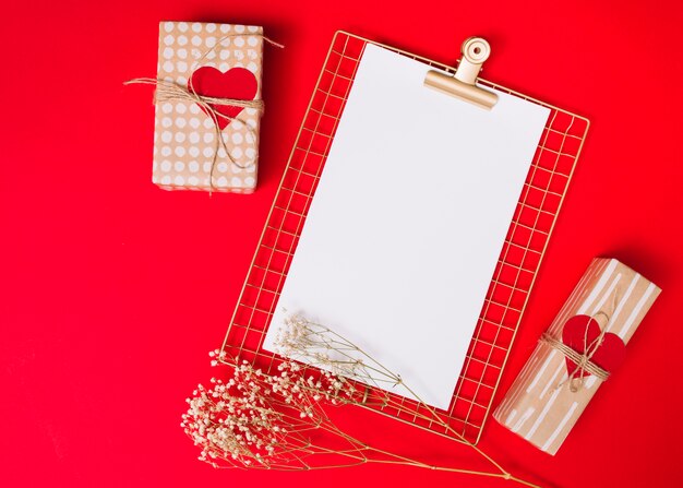 Present boxes with ornament hearts and clipboard near plant