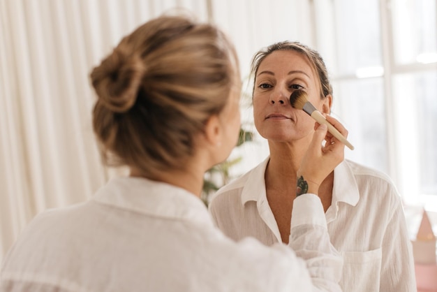 Pretty adult caucasian woman in white shirt uses services of makeup artist, getting ready for meeting. Natural beauty, skin care concept