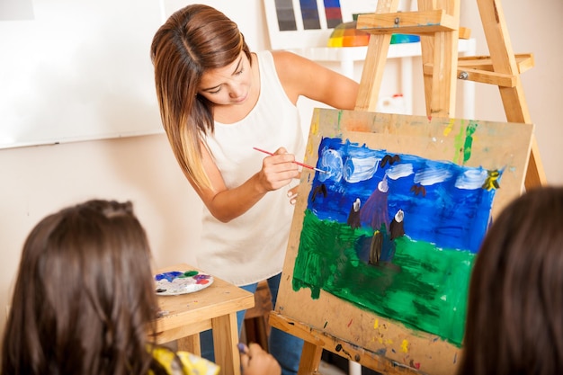 Free photo pretty art teacher helping a student with her painting during art class