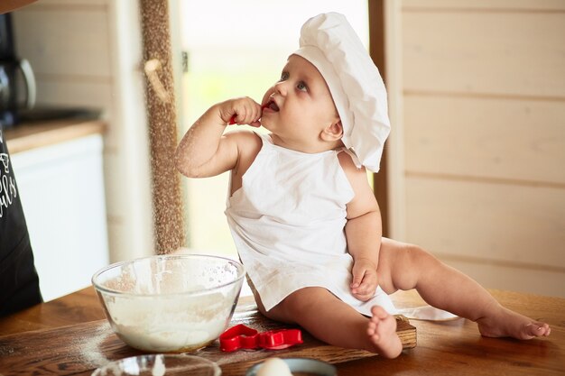 The pretty baby sits near plate with flour