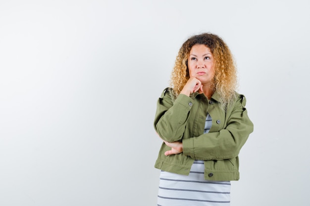 Pretty blond woman in green jacket propping chin on hand and looking pensive , front view.