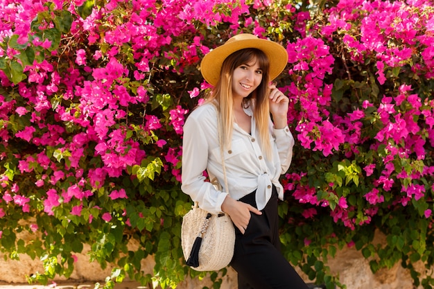 Pretty blond woman in straw hat posing over pink blooming tree in sunny spring day