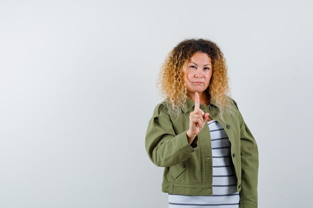 Pretty blond woman warning with index finger in green jacket and looking serious , front view.