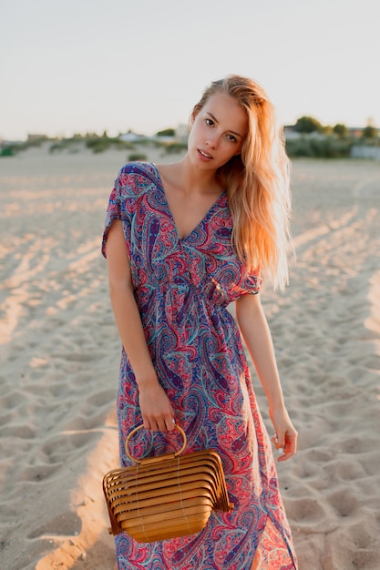 Pretty blond woman with bouquet of lavender walking on the beach. Sunset colors.