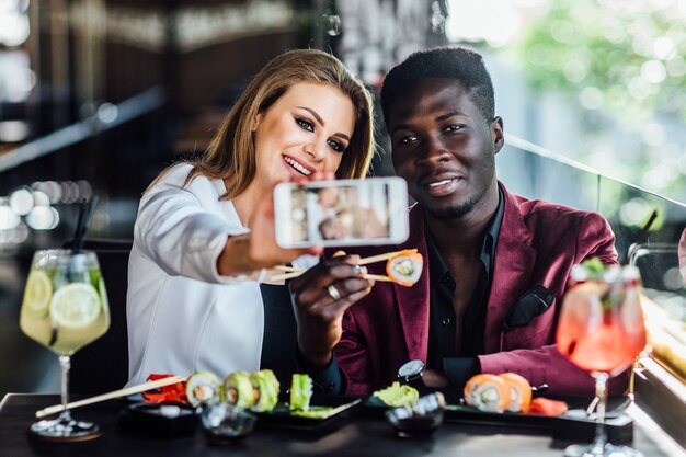 Pretty blonde girl taking a picture by the cell phone with sushi and mojito.