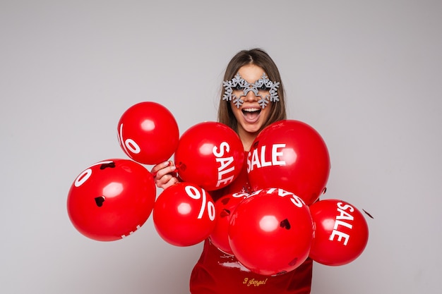 Free Photo pretty brunette woman in fancy glasses with snowflakes holding air balloons with sale word and percent sign.