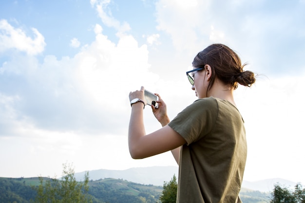 Pretty brunette woman traveling, taking photo of beautiful mountains view