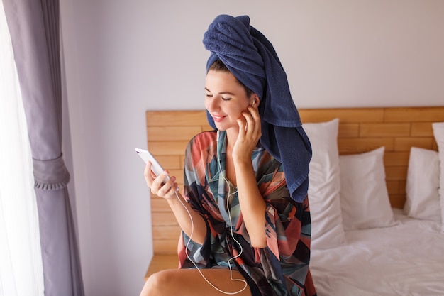 Free Photo pretty brunette woman wrapped in a shower towel using mobile phone while sitting on bed