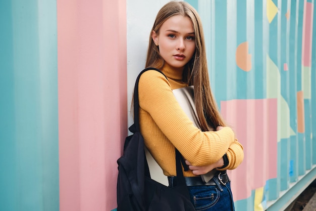 Free photo pretty casual student girl with laptop intently looking in camera over colorful background outdoor