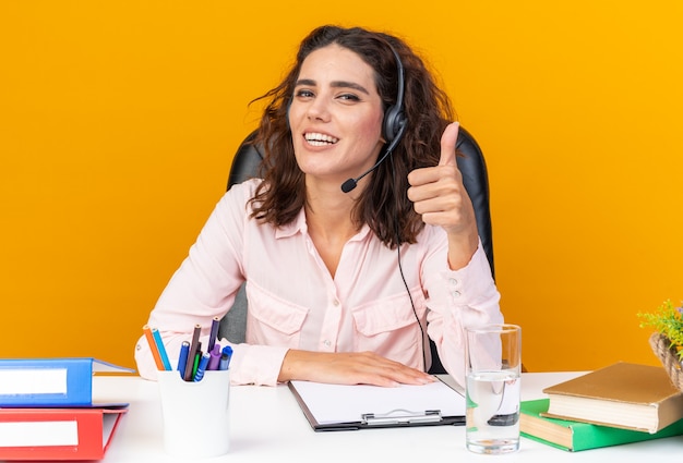 Free Photo pretty caucasian female call center operator on headphones sitting at desk with office tools 