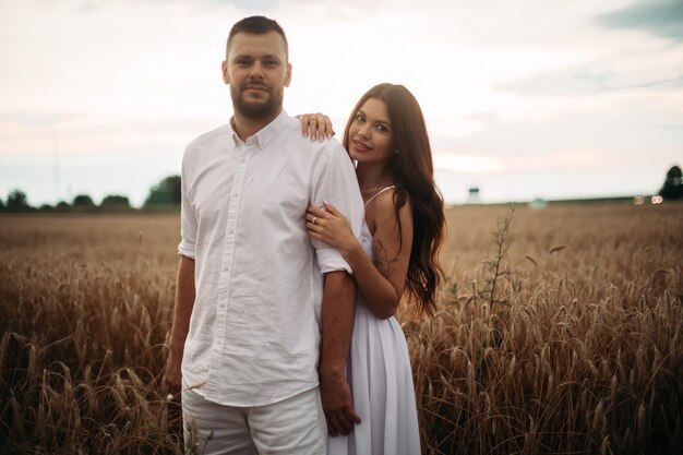 Pretty caucasian woman with long dark wavy hair in white dress hugs with beautiful man in white t-shirt and shorts