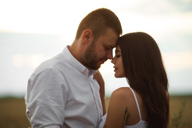 Pretty caucasian woman with long dark wavy hair in white dress hugs with beautiful man in white t-shirt and shorts