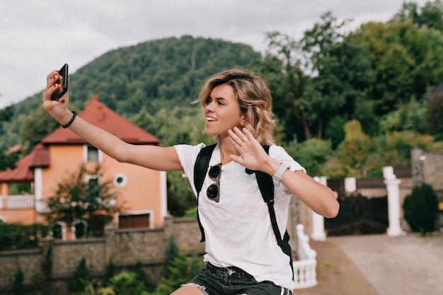 Free photo pretty charming traveler woman making selfie on smartphone over mountain in sunny good day. travel concept, vacation, trip