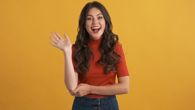 Pretty cheerful brunette girl happily waving hello on camera over colorful background Greeting expression