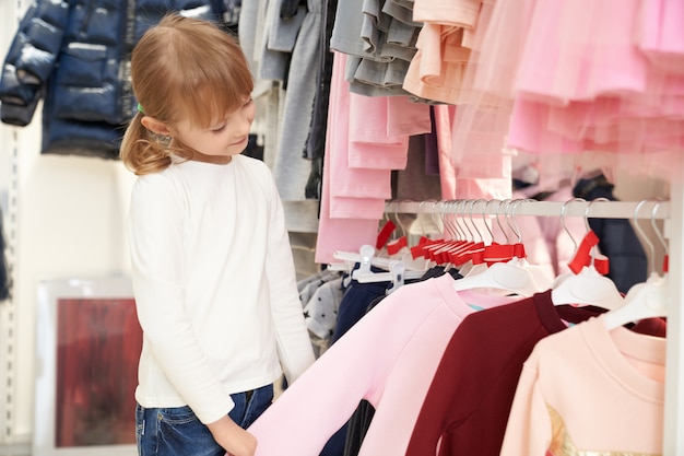 Free photo pretty child choosing clothing in store.