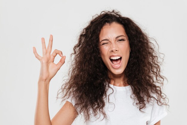 Pretty curly woman showing ok sign with open mouth