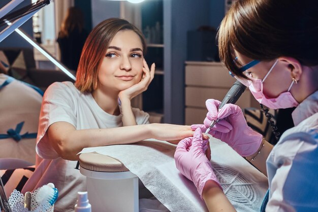 Pretty dreamy woman with tattoo got nail care from young dilligent manicurist.