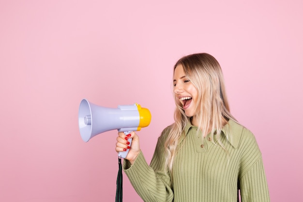 Free photo pretty european woman in casual sweater with megaphone on pink wall