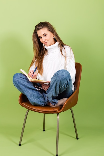 Free photo pretty european woman in casual white sweater isolated, cute happy sit on chair with notepad and pen