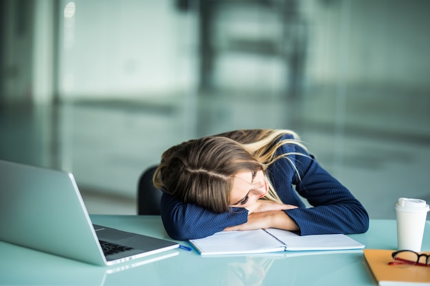 Pretty exhausted young businesswoman sitting at her desk sleeping in her office