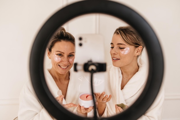 Pretty fair-skinned women use anti-wrinkle patches and take photo through ring lamp on tripod. Beauty procedure, morning ritual concept