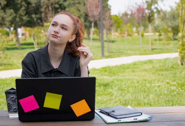 Pretty female freelancer working using laptop looking up thinking considering