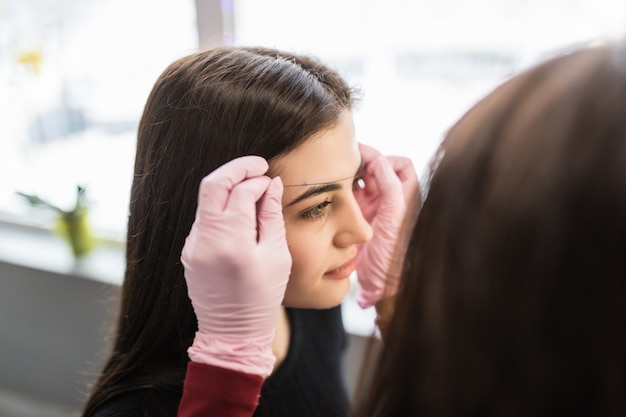 Pretty female master in white gloves determine eyebrow contour on young model