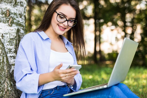 Pretty girl in blue jeans work with laptop and phone in citypark