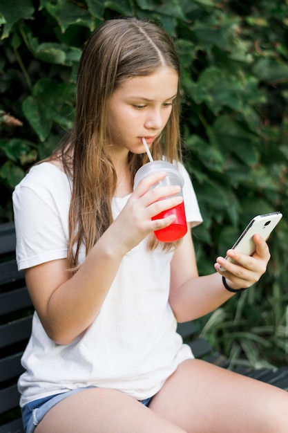 Pretty girl drinking juice while using smartphone at park