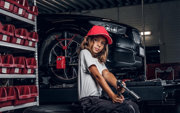 Free photo pretty girl is posing for photographer while sitting at dark auto service holding pneumatic drill.