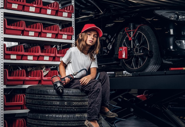 Free photo pretty girl is posing for photographer while sitting at dark auto service holding pneumatic drill.