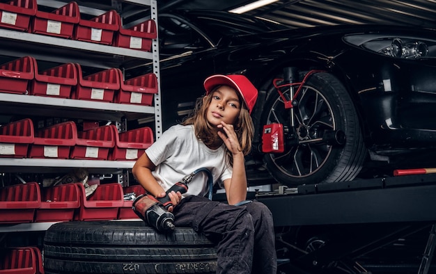 Free photo pretty girl is posing for photographer while sitting at dark auto service holding pneumatic drill.